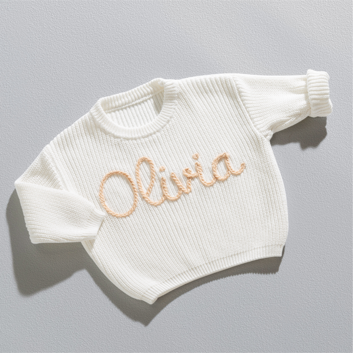 Personalisierter Strickpullover in Weiß mit dem Namen Olivia, handgestickt in Sand